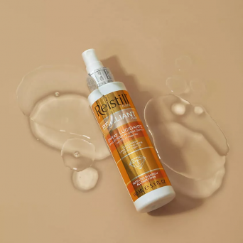 Reistill Brilliant Plus gloss spray 150 ml lying on beige surface with liquid drops, shine spray with organic argan oil for all hair types